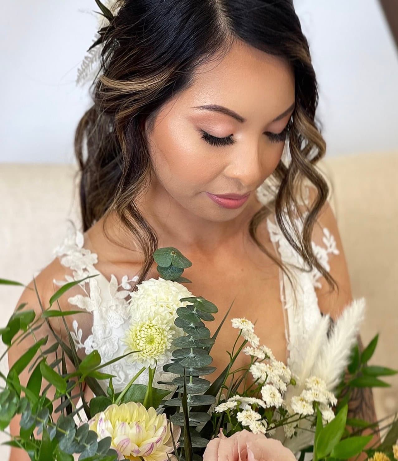 Bride with soft glam makeup featuring pink lips and defined brows, wearing wavy highlighted hair with side-swept styling.